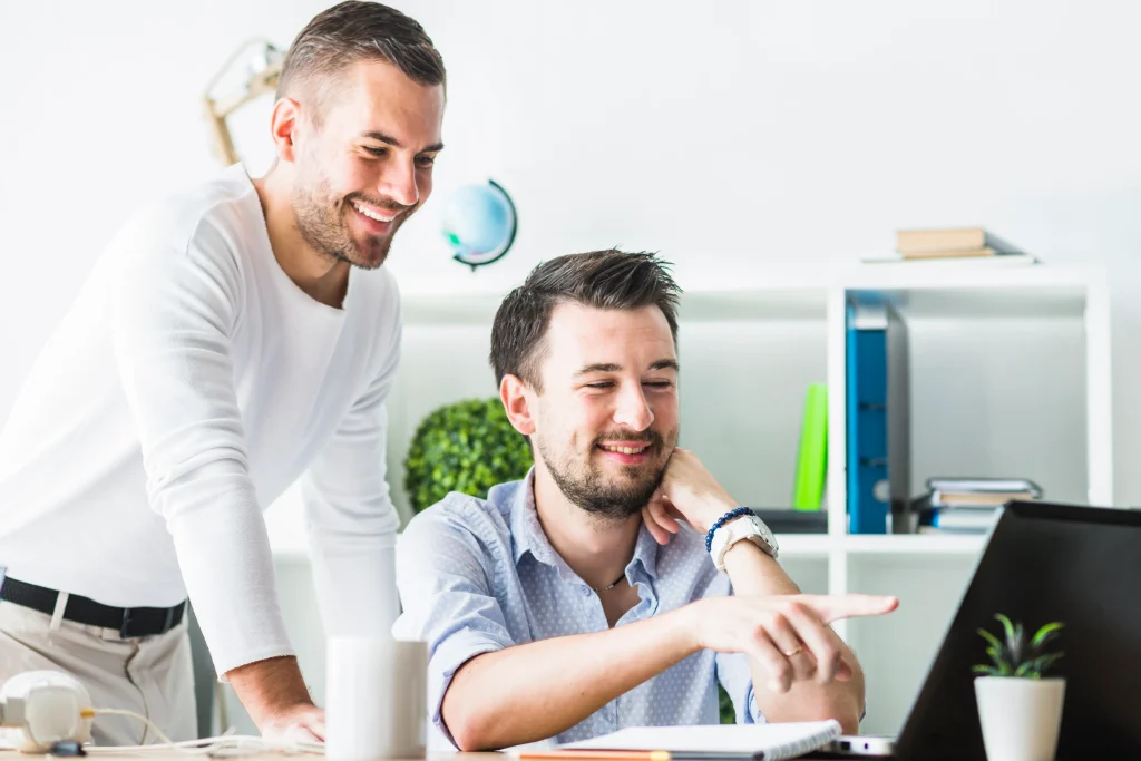 two smiling young businessmen looking laptop screen